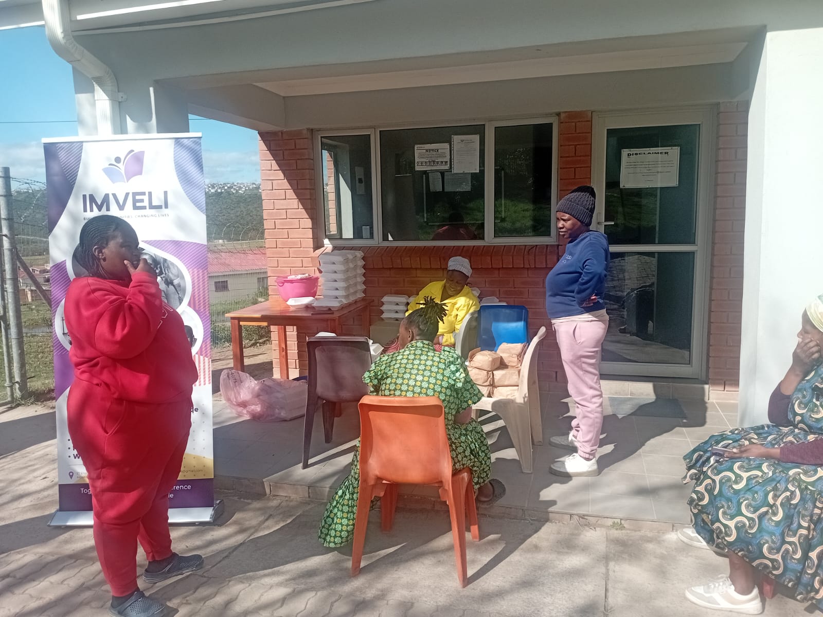 Imveli team members pack meal containers on a table beside the Imveli banner