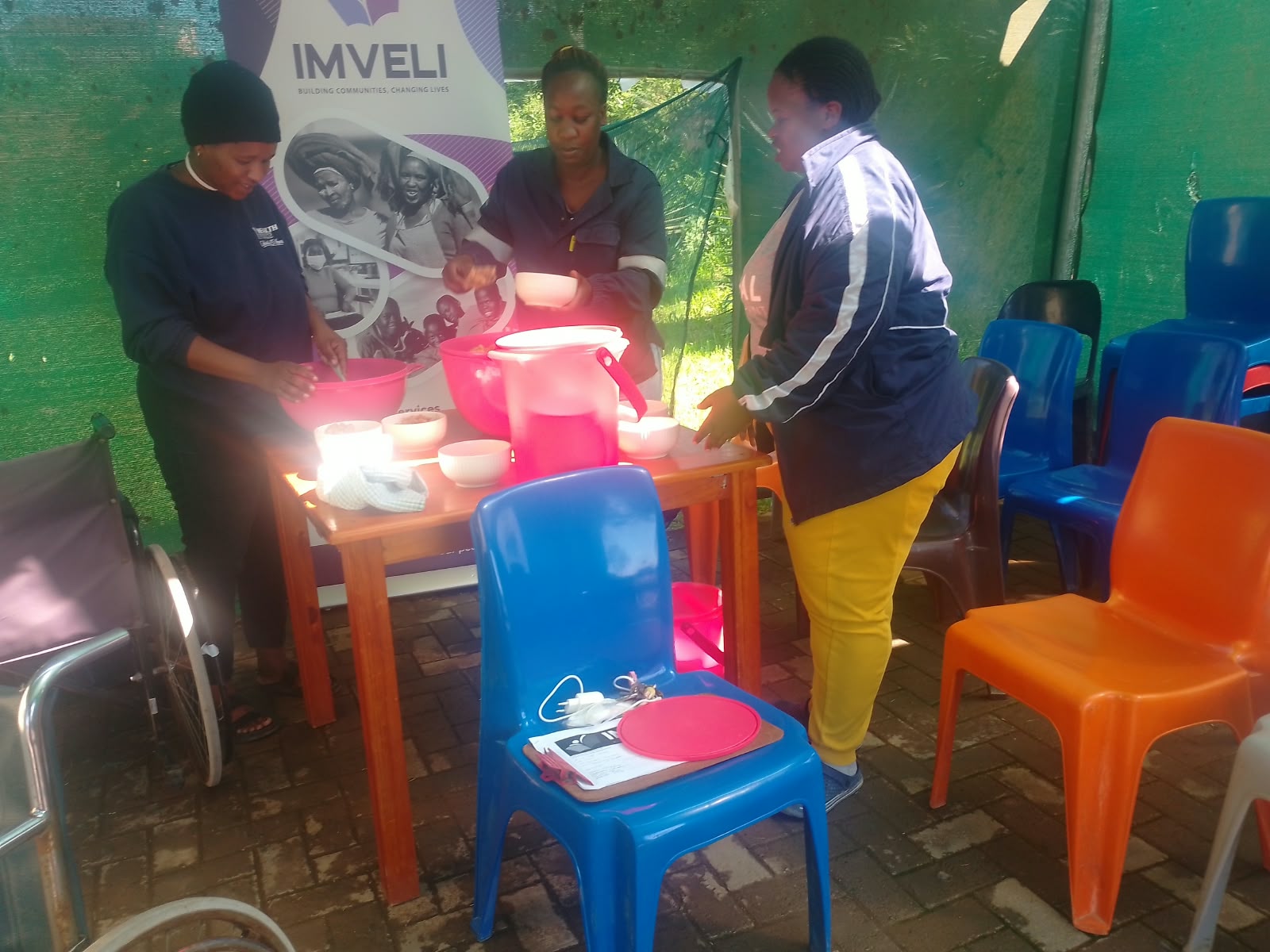 Imveli team members preparing and serving meals from large bowls at a serving table under a canopy
