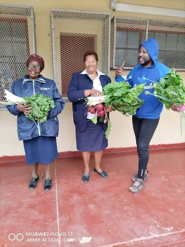 Three community members holding mixed vegetable harvests