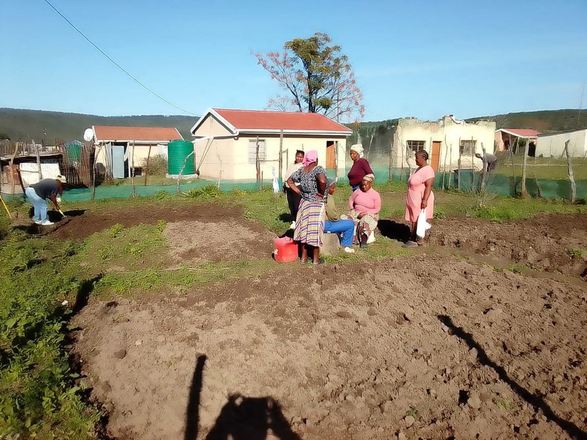 Community members working together in the garden with village houses behind them