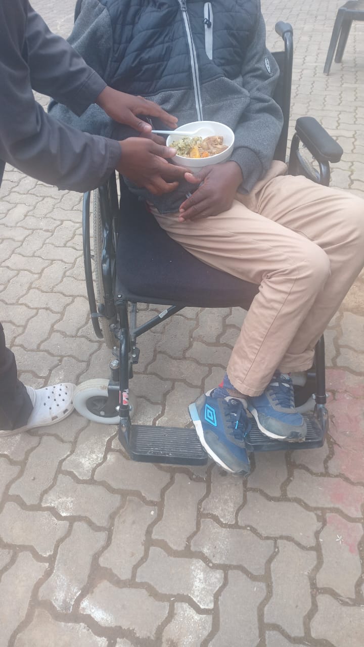 A community member seated in a wheelchair receiving a prepared meal from a support team member