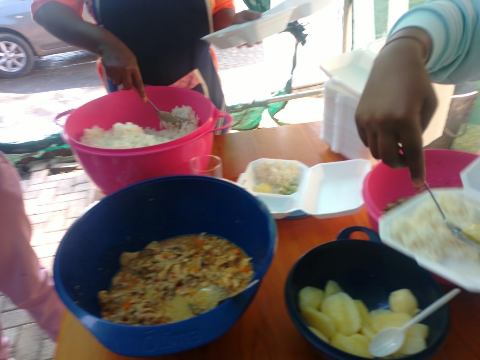 Close view of rice, a cooked dish and potatoes in large bowls being portioned into meal containers