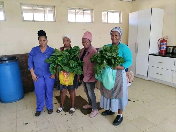 Four women holding fresh spinach and chard harvests indoors